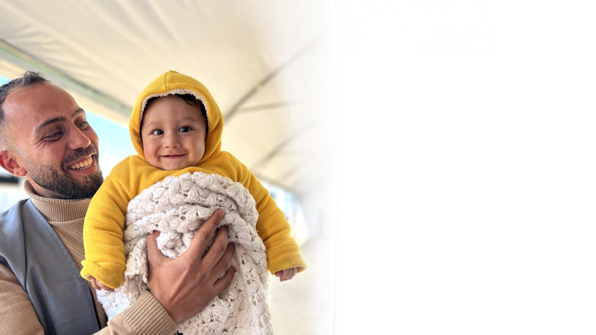 Bimbo sorridente in braccio a un operatore di Save the Children